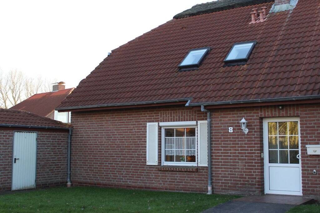 A brick house with a red-tiled roof, a white door, and a small window with shutters.