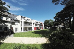 Un immeuble résidentiel à plusieurs étages, avec une allée pavée et une pelouse bien entretenue.