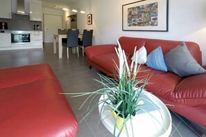 Ein modernes Wohnzimmer mit einem roten Sofa, einem kleinen runden Tisch mit einer Pflanze und einem Essbereich im Hintergrund.
