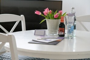 A round white table with a white chair, a vase with pink flowers, a bottle of water, a bottle of alcohol, and a glass. - Holiday apartment with 1 bedroom (Westerland\/ Sylt)