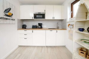 A compact kitchen with white cabinets, a microwave, a coffee maker, and a sink. - Holiday apartment with 1 bedroom (Westerland\/ Sylt)