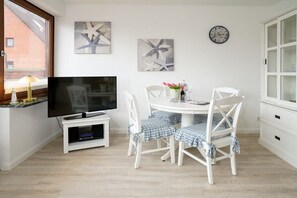 A dining area with a round table, white chairs, and artwork on the walls. - Holiday apartment with 1 bedroom (Westerland\/ Sylt)