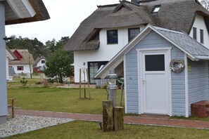 Ein Haus mit Strohdach, eine kleine Werkstatt und ein gepflasterter Weg.
