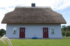 Ein Haus mit einem Strohdach, zwei roten Türen und einem kleinen Garten davor.