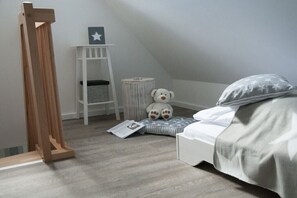 Ein Kinderzimmer mit einem Bett, einer kleinen weißen Regal und einem Teddybär sowie einer Lesematte.