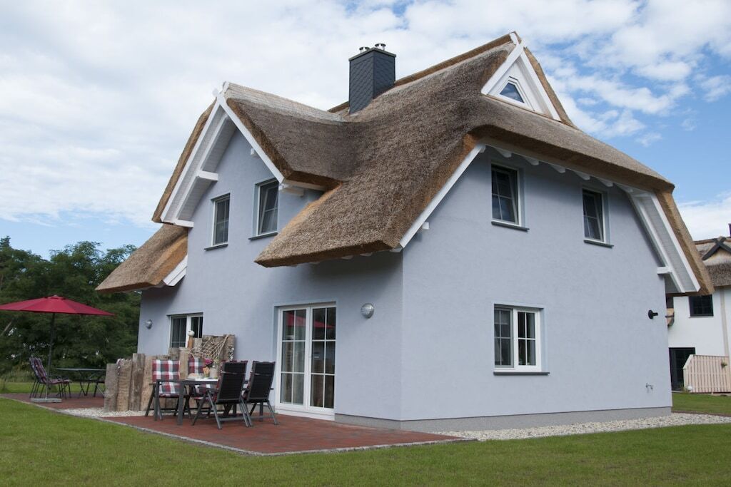A house with a unique thatched roof, a covered patio with outdoor furniture, and a well-maintained lawn.