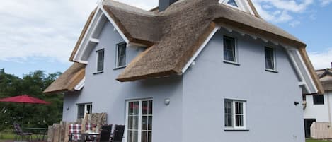 A house with a unique thatched roof, a covered patio with outdoor furniture, and a well-maintained lawn.