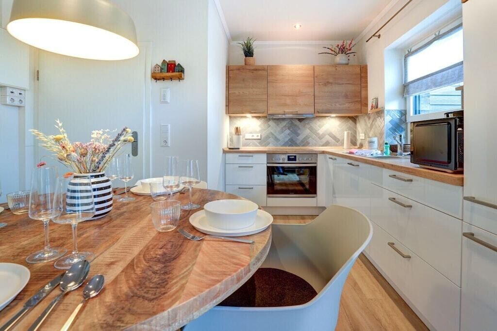 A modern kitchen with wooden cabinets, a built-in oven, and a dining area with a round table and chairs.