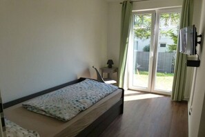 Ein Schlafzimmer mit einem Einzelbett, einem kleinen Nachttisch mit Lampe und einem an der Wand montierten Fernseher.