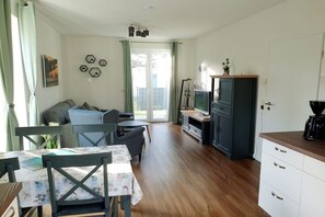 Ett kompakt bostadsutrymme med en matplats, en soffa, en tv och ett litet kök.