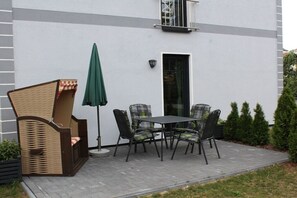 Eine Terrasse im Freien mit Tisch und Stühlen, einer Rattanbank und einem grünen Sonnenschirm.