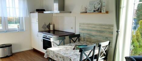 A compact kitchen with a dining table, chairs, and a window with curtains.