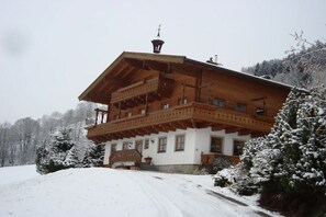 A wooden chalet with a balcony, surrounded by snow-covered trees. - Ebnerbauer Apartment 1 (Piesendorf)