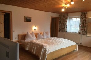 A bedroom with a wooden bed, a nightstand, a wall-mounted light, a window with curtains, and a radiator. - Ebnerbauer Apartment 1 (Piesendorf)