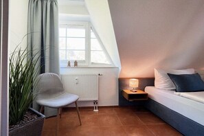 A modern bedroom with a bed, a chair, a nightstand, a lamp, a window, and a radiator. - Holiday apartment with 2 bedrooms (Dierhagen)