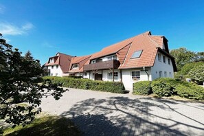 Ein Wohngebäude mit geneigtem Dach, zahlreichen Fenstern und einer gepflasterten Auffahrt.