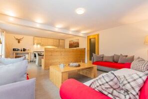 Ein modernes Wohnzimmer mit einem roten Sofa, einem Holztisch und einer Küchenzeile mit Holdekor und einem aufgehängten Hirschkopf.