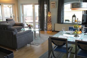 A modern living room with a grey sofa, a glass coffee table, and a dining area with a glass table and chairs. - Residence Juliana 52 (Julianadorp)