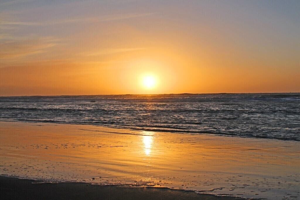 Een strand met de ondergaande zon aan de horizon, weerspiegeld in het water.