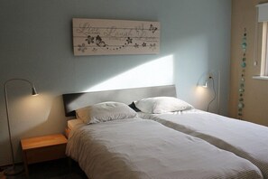 A bedroom with two beds, a bedside table, a wall-mounted artwork, and a window with blinds. - Residence Juliana 52 (Julianadorp)