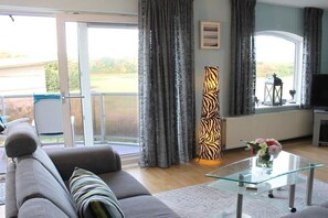 A living room with a sofa, a glass coffee table, a zebra-patterned floor lamp, and a television. - Residence Juliana 52 (Julianadorp)