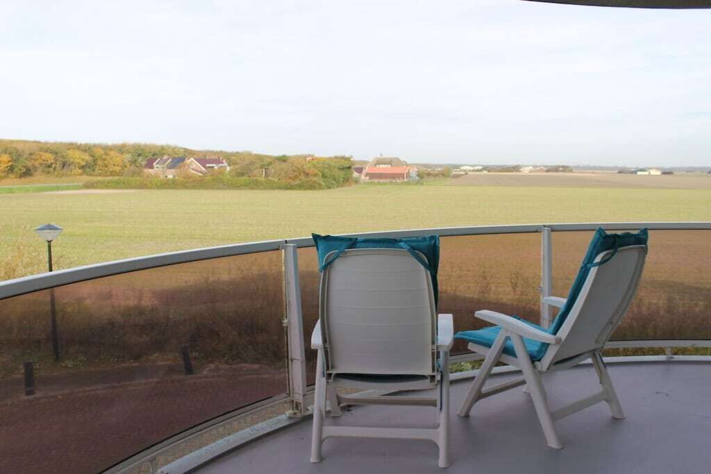 Un balcon avec deux chaises et une table, donnant sur un champ et des maisons.