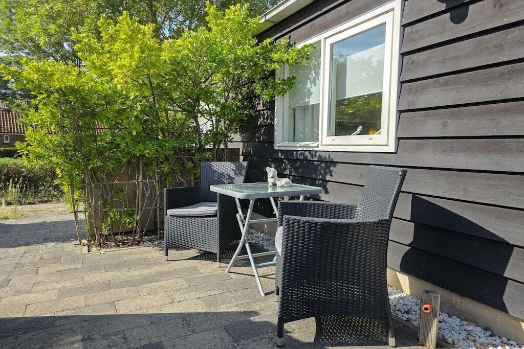 Eine Terrasse im Freien mit Korbmöbeln, einem Tisch und einem Fenster mit Blick auf einen Garten.