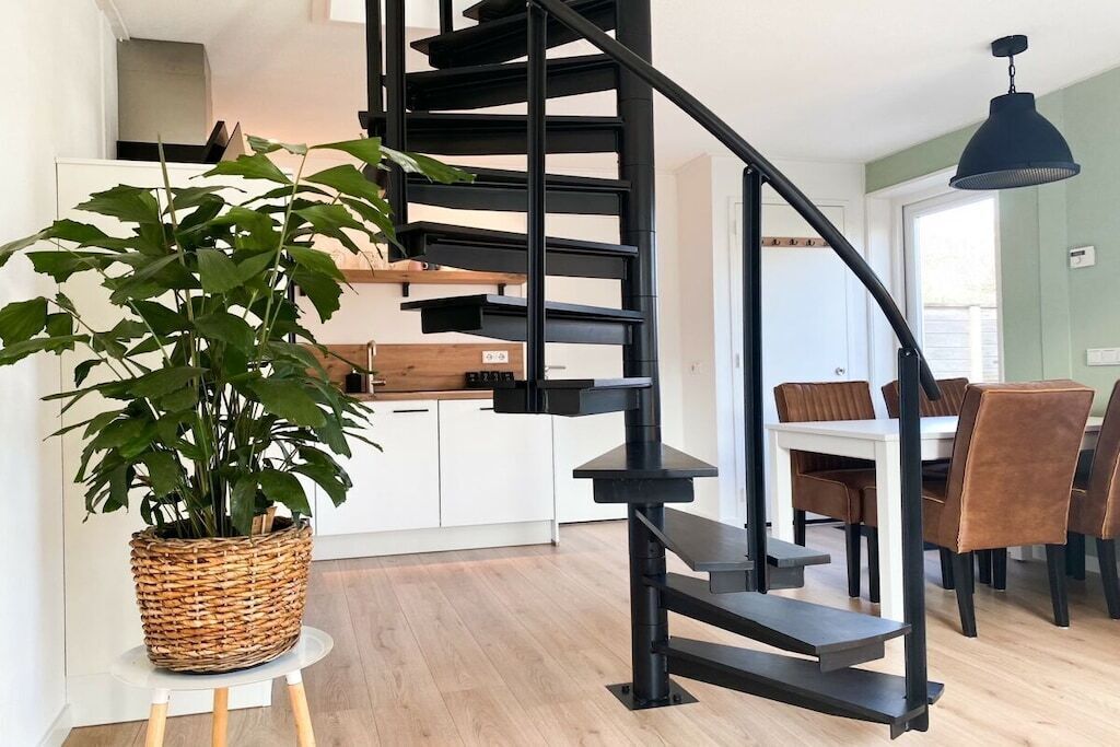 A modern kitchen with white cabinets, a black spiral staircase, and a dining area with brown chairs.