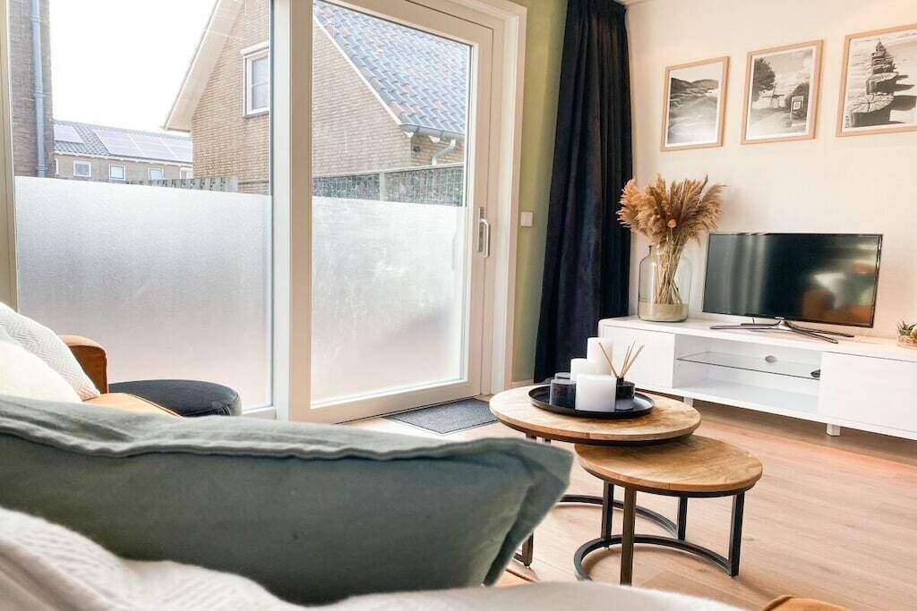 A modern living room with a sofa, a coffee table, a TV on a white cabinet, and a sliding glass door leading to a balcony.
