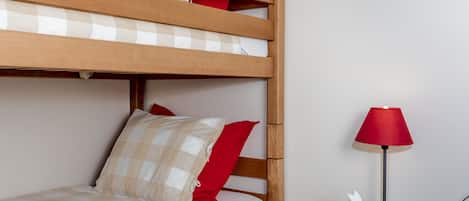 A bunk bed with a checkered bedspread and red pillows, a bedside table with a red lamp, and a white rabbit decoration.