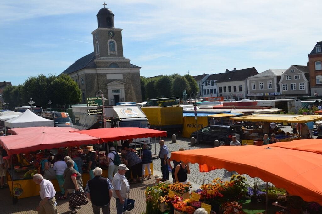 Un mercado al aire libre con varios puestos y una iglesia destacada al fondo.