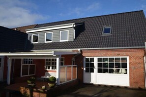 Ein zweigeschossiges Haus mit überdachter Terrasse, einer Garage und einem kleinen Fenster im Obergeschoss.