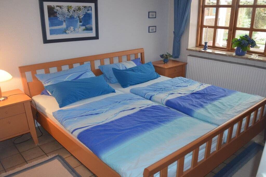 A bedroom with a wooden bed, a nightstand, a window with curtains, and a framed picture on the wall.