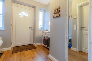 A hallway with a white door, a small window, a wall-mounted sign, and a white cabinet with shelves. - Thatched-roof house Frisian dream (Garding)