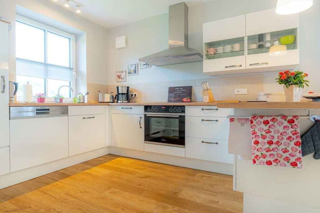 A modern kitchen with white cabinets, a built-in oven, and a window providing natural light.
