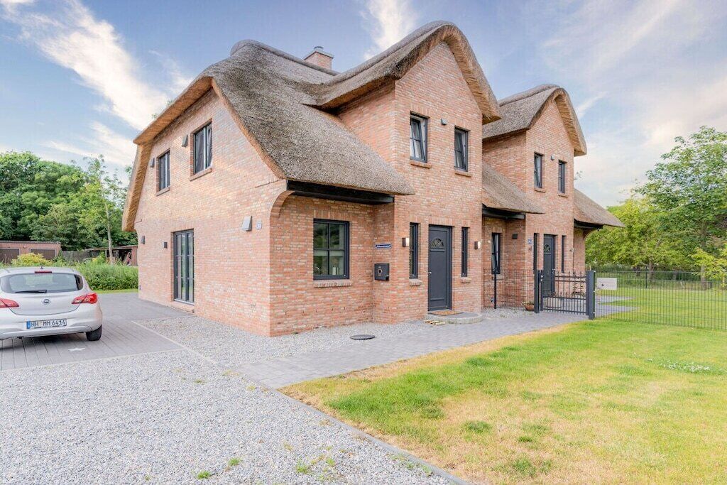 A two-story brick building with a thatched roof, a car parked in front, and a grassy area to the right.