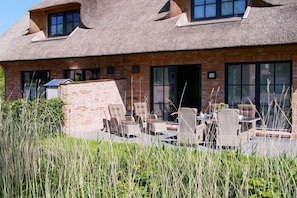 A brick building with a thatched roof, outdoor seating area with wicker furniture, and a brick wall with windows. - Thatched-roof house Frisian dream (Garding)