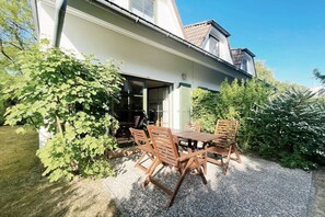 Una veranda con tavolo e sedie, circondata dal verde e da un edificio con tetto spiovente.