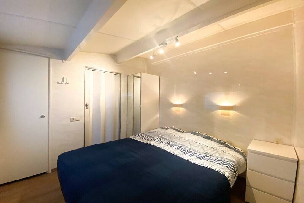 Un dormitorio con cama, mesita de noche, armario e iluminación de pared.