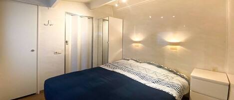 Un dormitorio con cama, mesita de noche, armario e iluminación de pared.