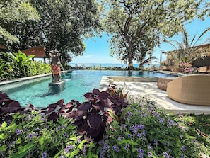 A pool area with a statue, surrounded by lush greenery and a view of the sea.
