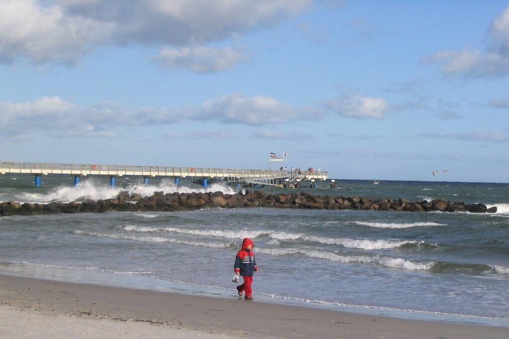 Une plage avec des vagues, une jetée et une personne qui se promène.