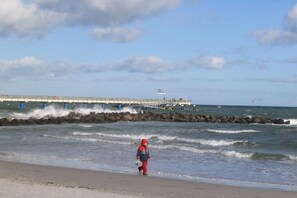 Ein Strand mit Wellen, einem Steg und einer Person, die spazieren geht.