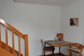 Ein Zimmer mit einer Holztreppe, einem Tisch mit Stühlen und einem gerahmten Bild an der Wand.
