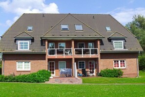 Une maison à deux étages avec un porche à l’avant, une terrasse couverte et un petit jardin.
