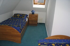 Une chambre avec un lit simple, une table de chevet, une lampe et une fenêtre.