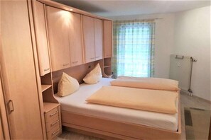 Un dormitori amb un llit, un armari de fusta i una finestra amb cortines.