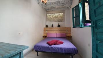 A bedroom with a wooden headboard, a purple bedspread, and a red towel.