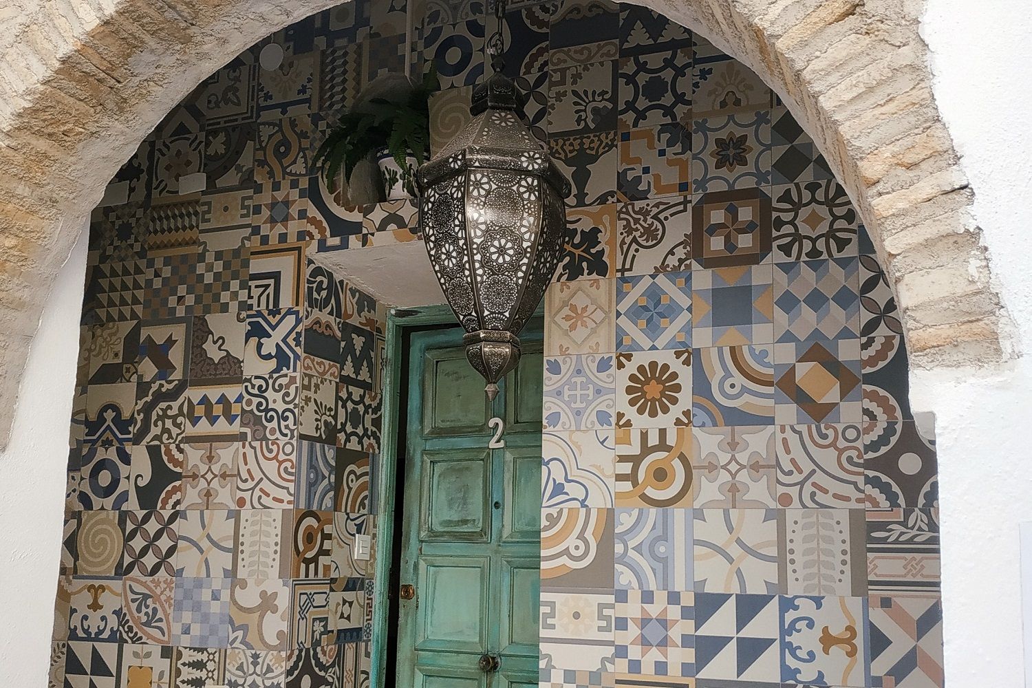 Ein Durchgang mit einer grünen Tür, umgeben von einer Wand mit verschiedenen geometrischen und floralen Mustern.