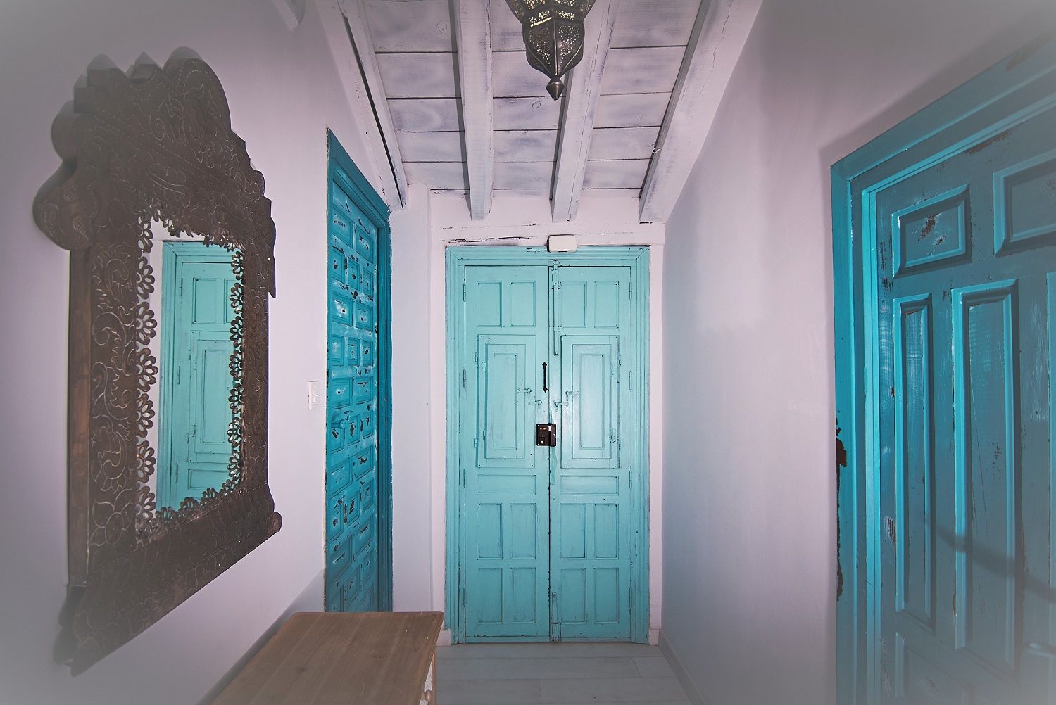A hallway with a wooden bench, a decorative mirror, and three doors with a teal color scheme.